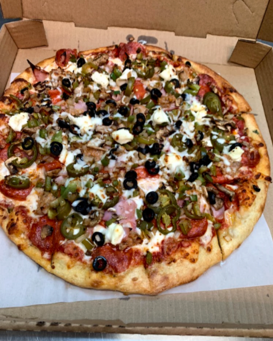 Cheese pizza topped with black olives, green olives, jalapeños, and diced onions in a cardboard pizza box