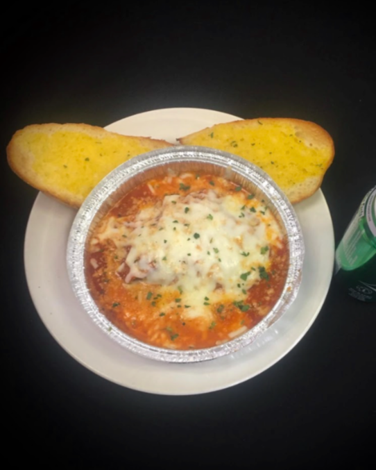 Baked Italian shrimp and cheese in a foil container, served with slices of garlic bread and a can of Sprite on a black table.