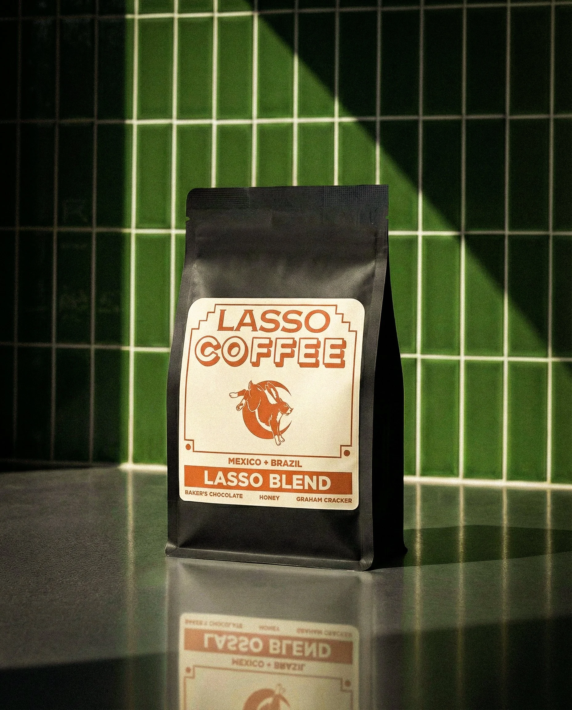 A black bag of Lasso Coffee Lasso Blend on a reflective countertop, with green tiled wall in the background.