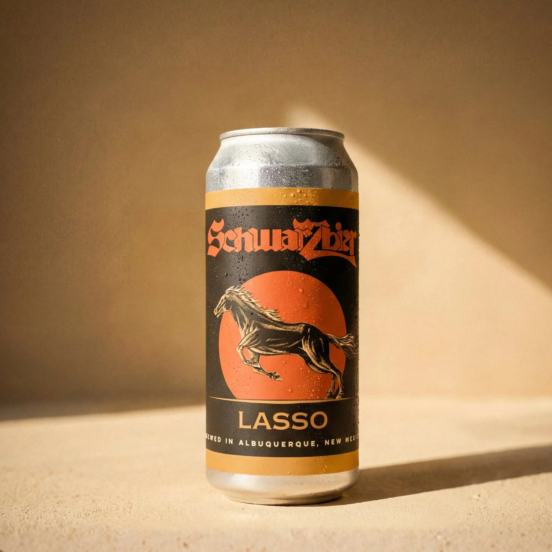 A can of Schwartz beer with a black and orange label featuring a running horse and the text "Lasso". The can is on a light surface with a gradient background.