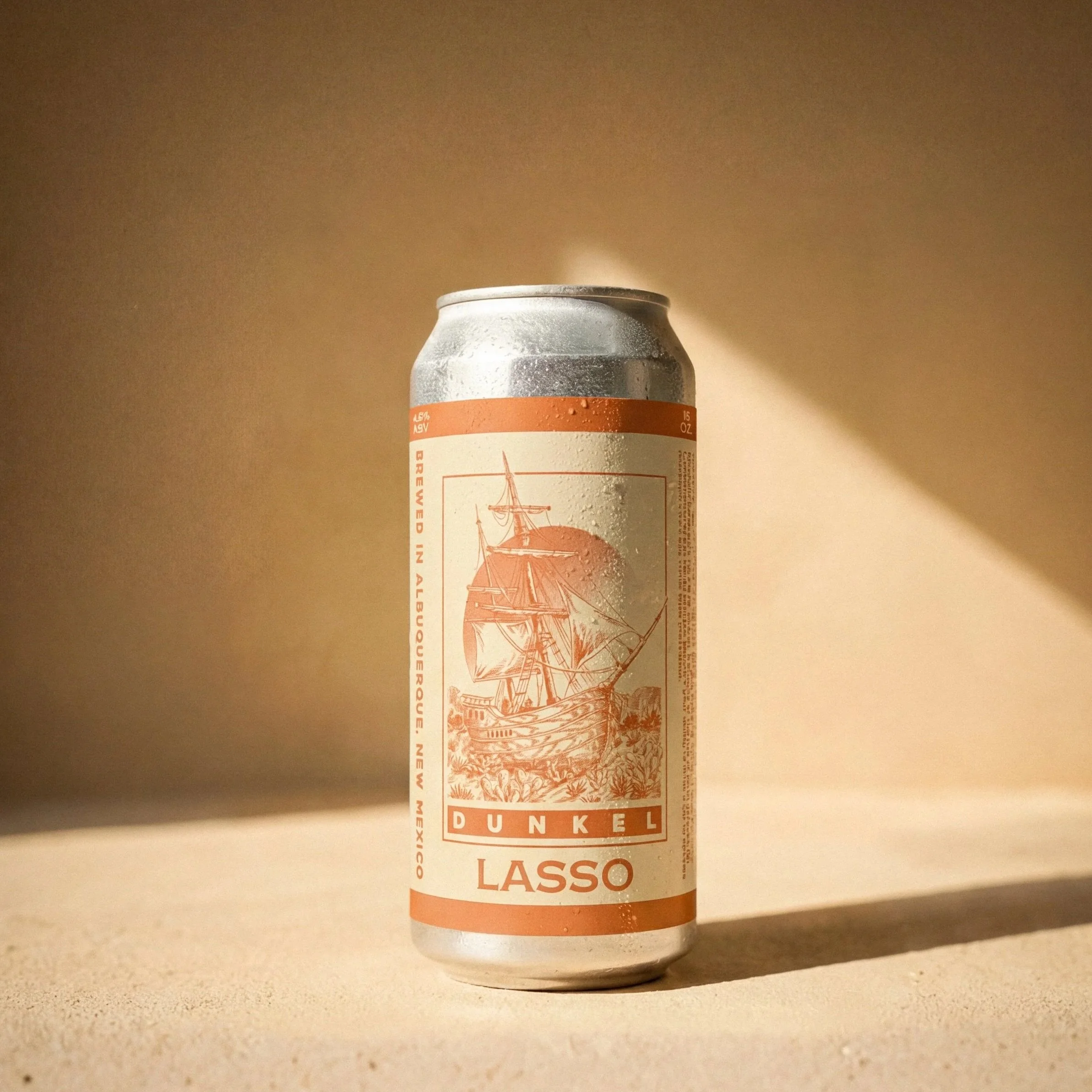 A can of Dunkel Lasso beer with a ship illustration on the label, placed on a light-colored surface with a shadow and beige background.