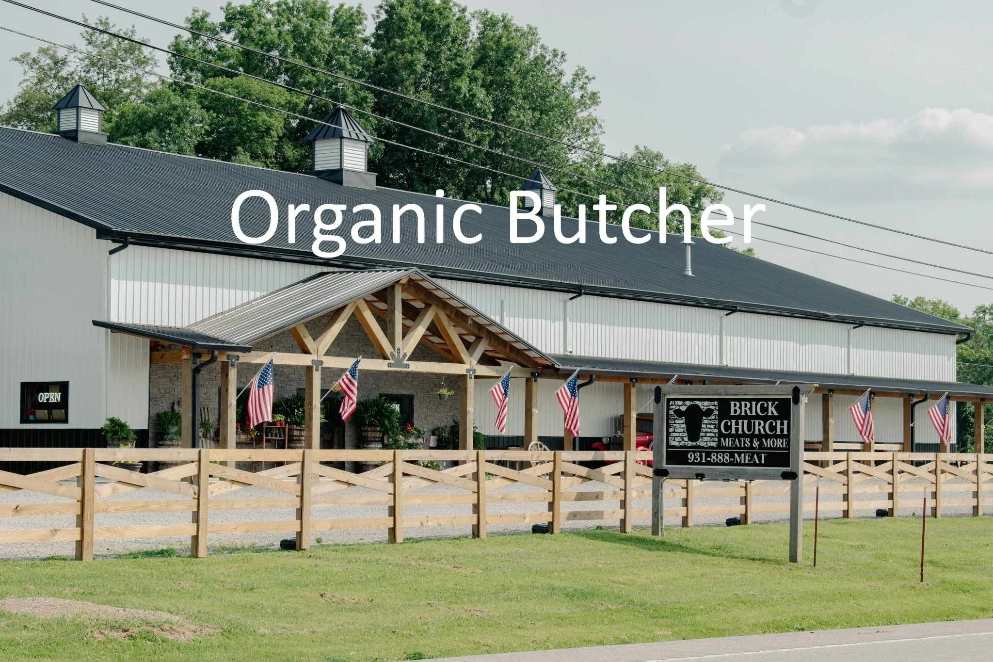 An outdoor view of a building with a sign for organic meats that reads "Brick Church Meats & More," decorated with American flags.