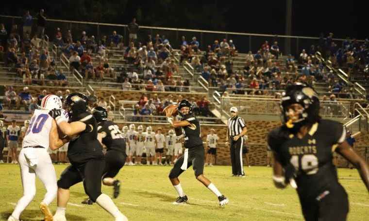 A nighttime American football game with players on the field and spectators in the stands