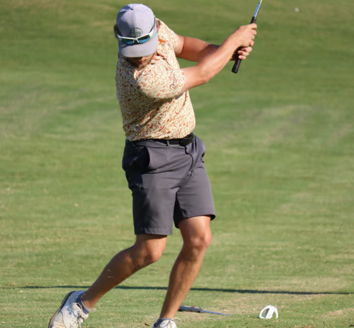 A man playing golf on a green field, swinging a golf club in Pulaski, TN country club.