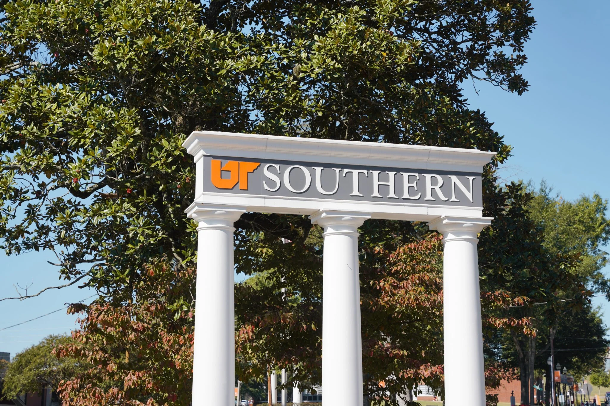Sign for University of Tennessee Southern with the UT logo, supported by three white columns, in front of trees and a city street.