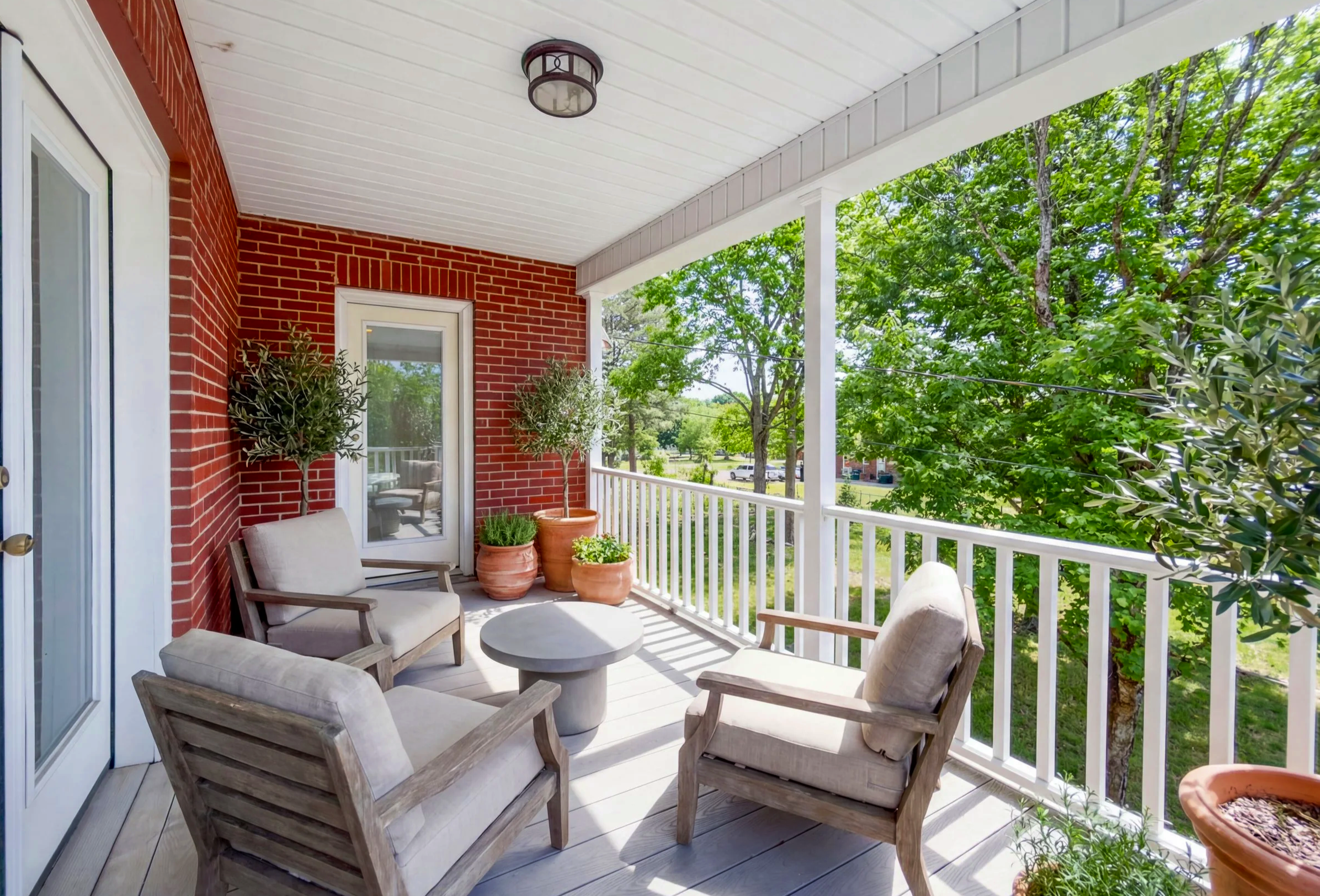 Cozy balcony with outdoor furniture, potted plants, and a view of green trees.