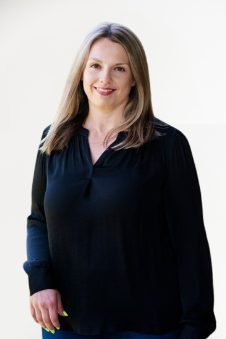 A woman with shoulder-length light brown hair, wearing a dark long-sleeve blouse, standing against a white background and smiling at the camera.