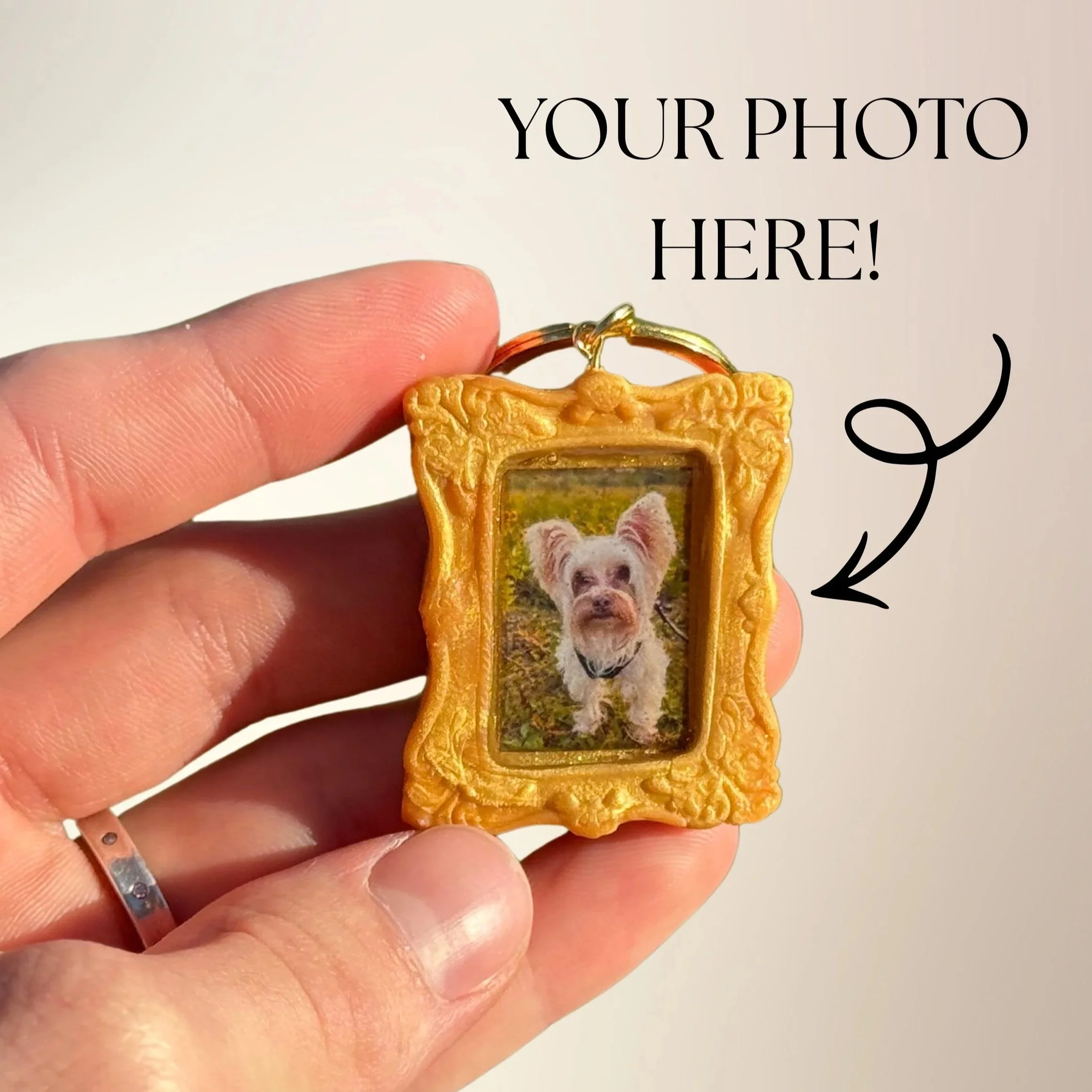 A close-up of a hand holding a dog-themed keychain with a picture of a small white dog inside a decorative golden frame. Text on the image reads 'Your Photo Here!' with an arrow pointing to the photo.