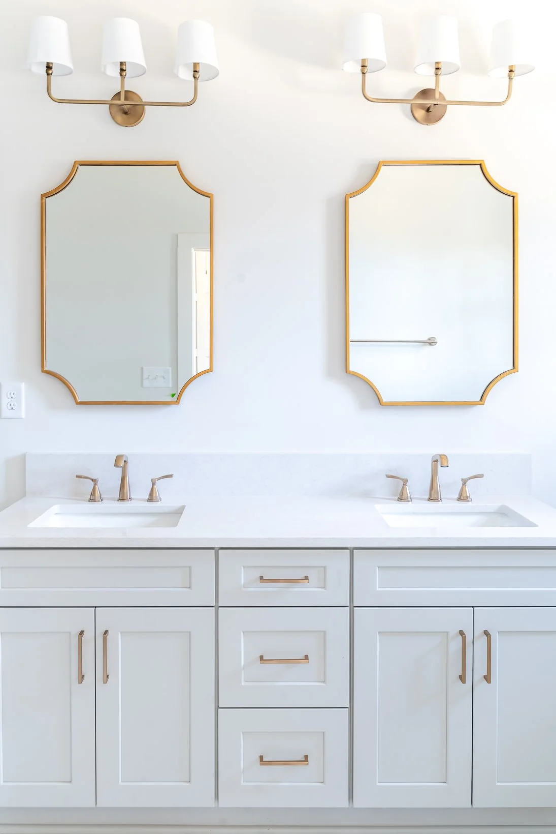 Bathroom vanity with two sinks, white countertops, gold hardware, and two mirrors above, with a gold light fixture above.