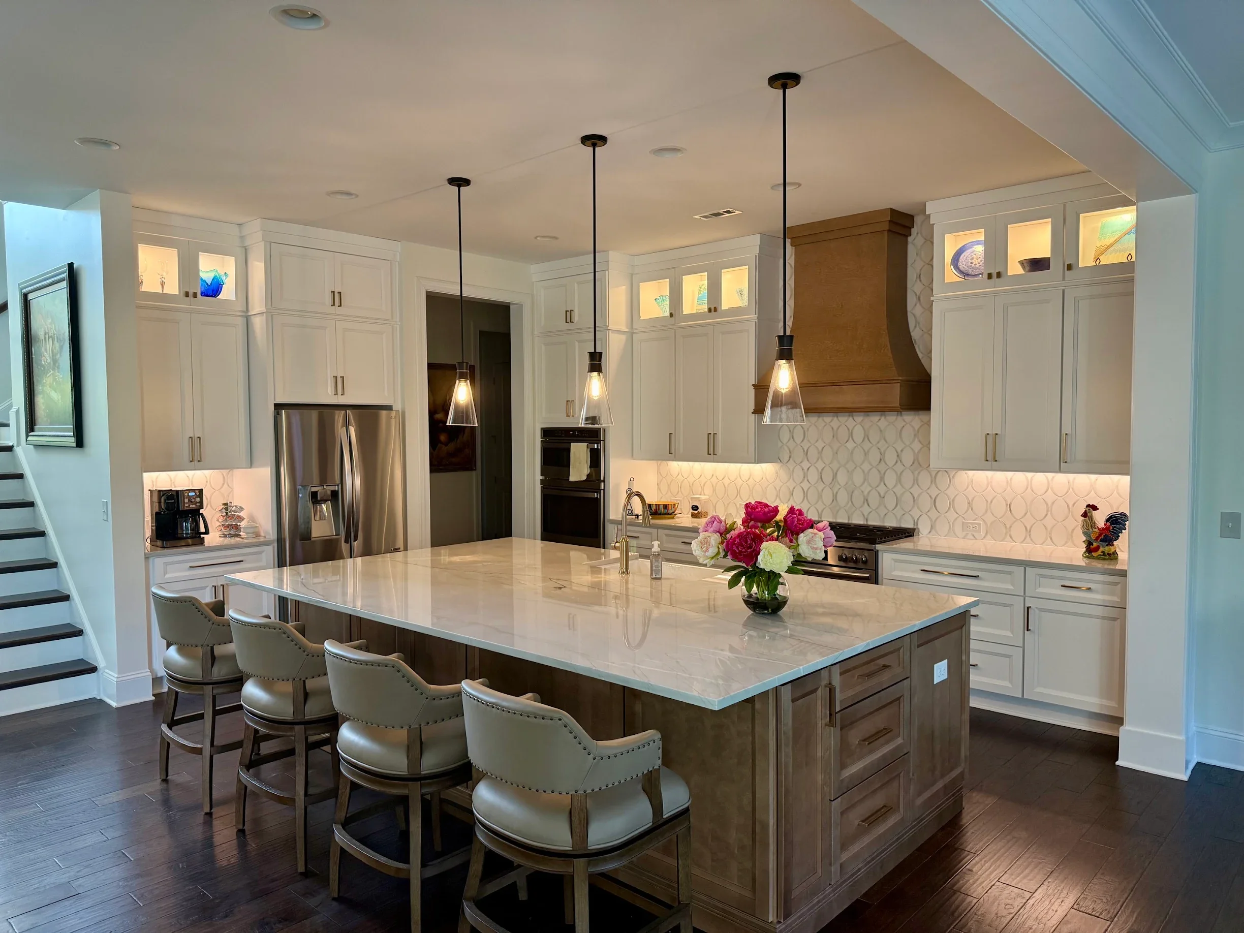 Modern kitchen with white cabinets, a large marble island, pendant lights, a stainless steel refrigerator, and a vase of pink and white flowers on the island.