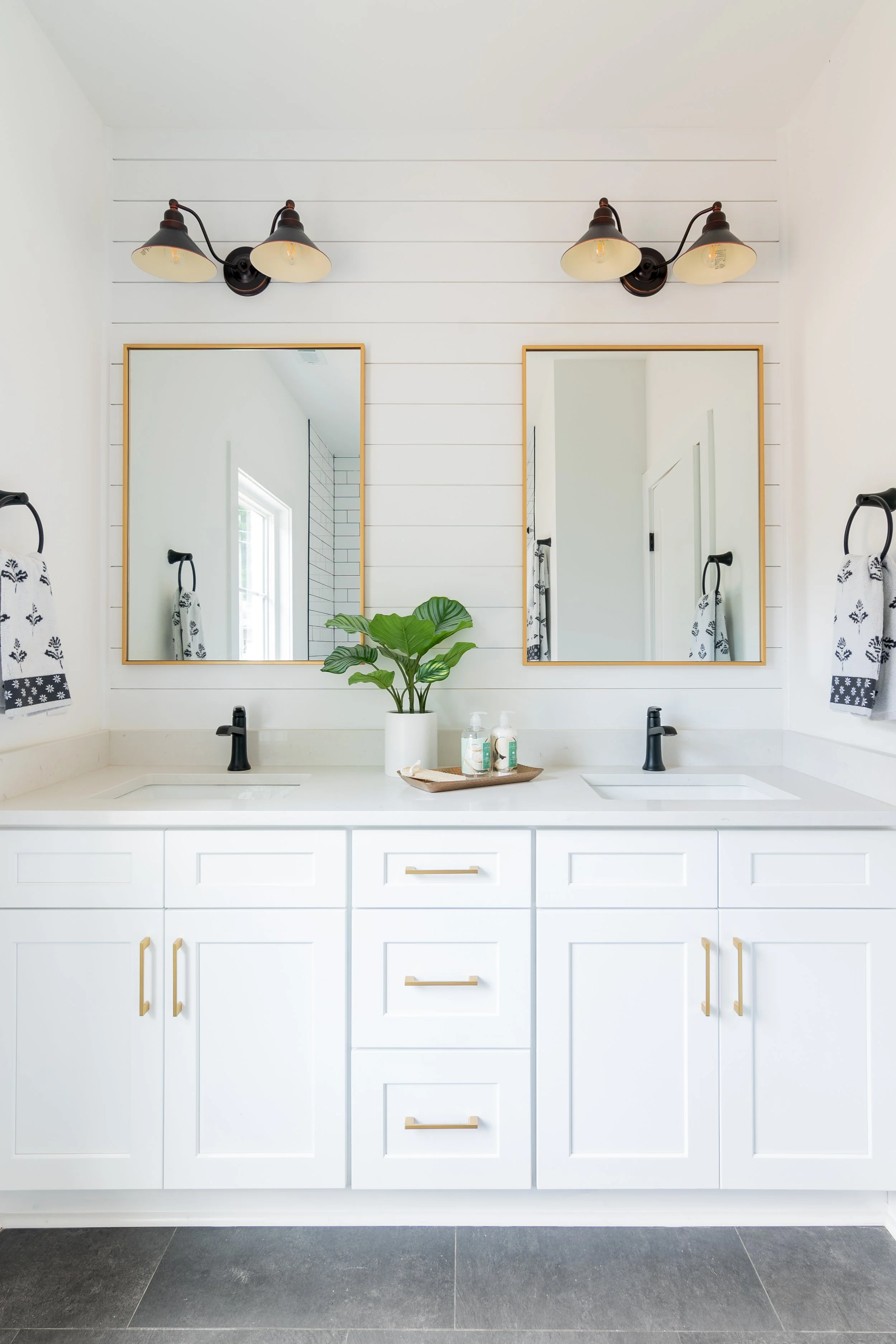 Bathroom vanity area with white cabinets, two black sinks, area for two mirrors, and black and white towels hanging on each side.