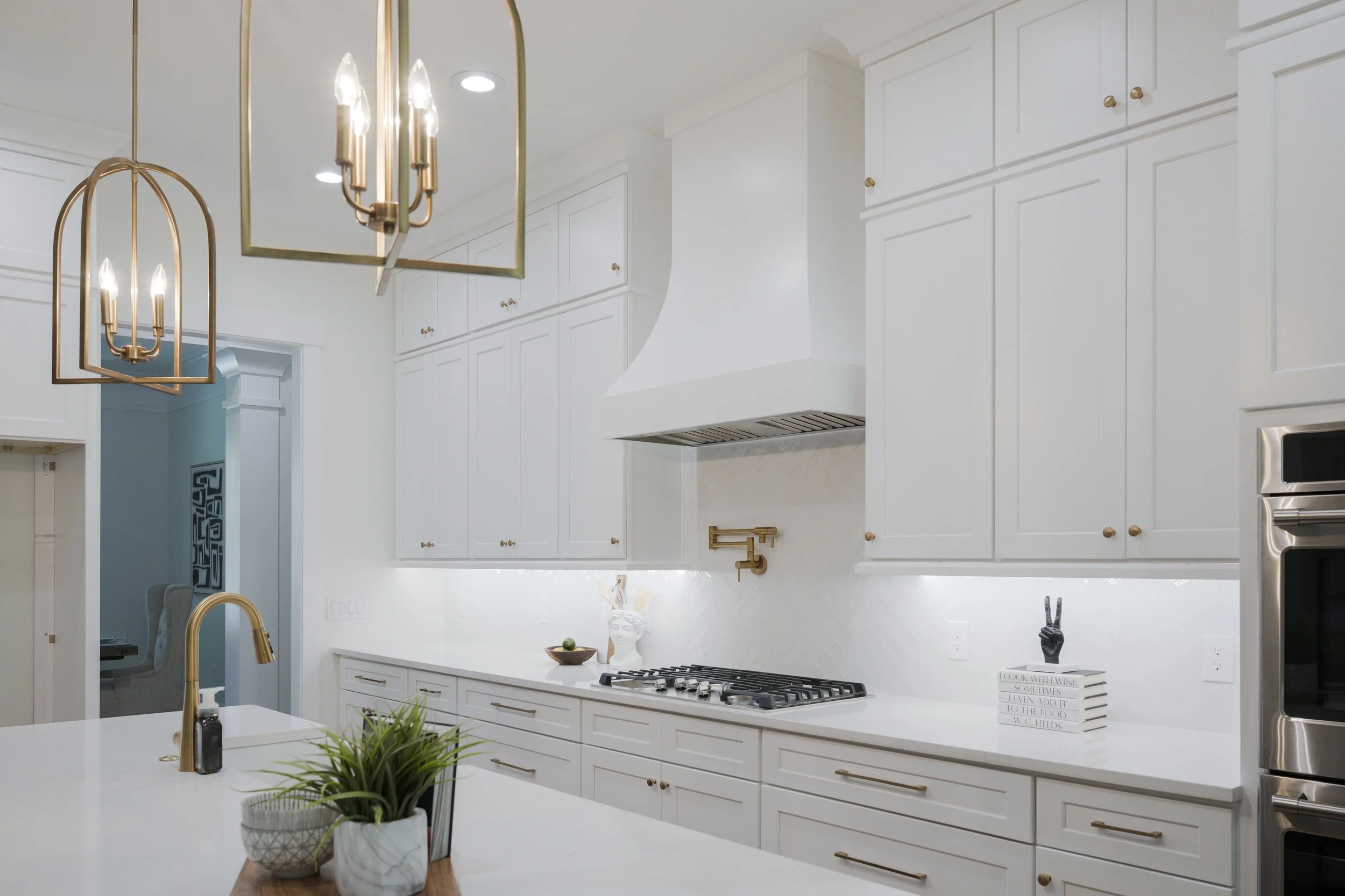 Modern white kitchen with gold hardware, decorative objects, and pendant lighting.