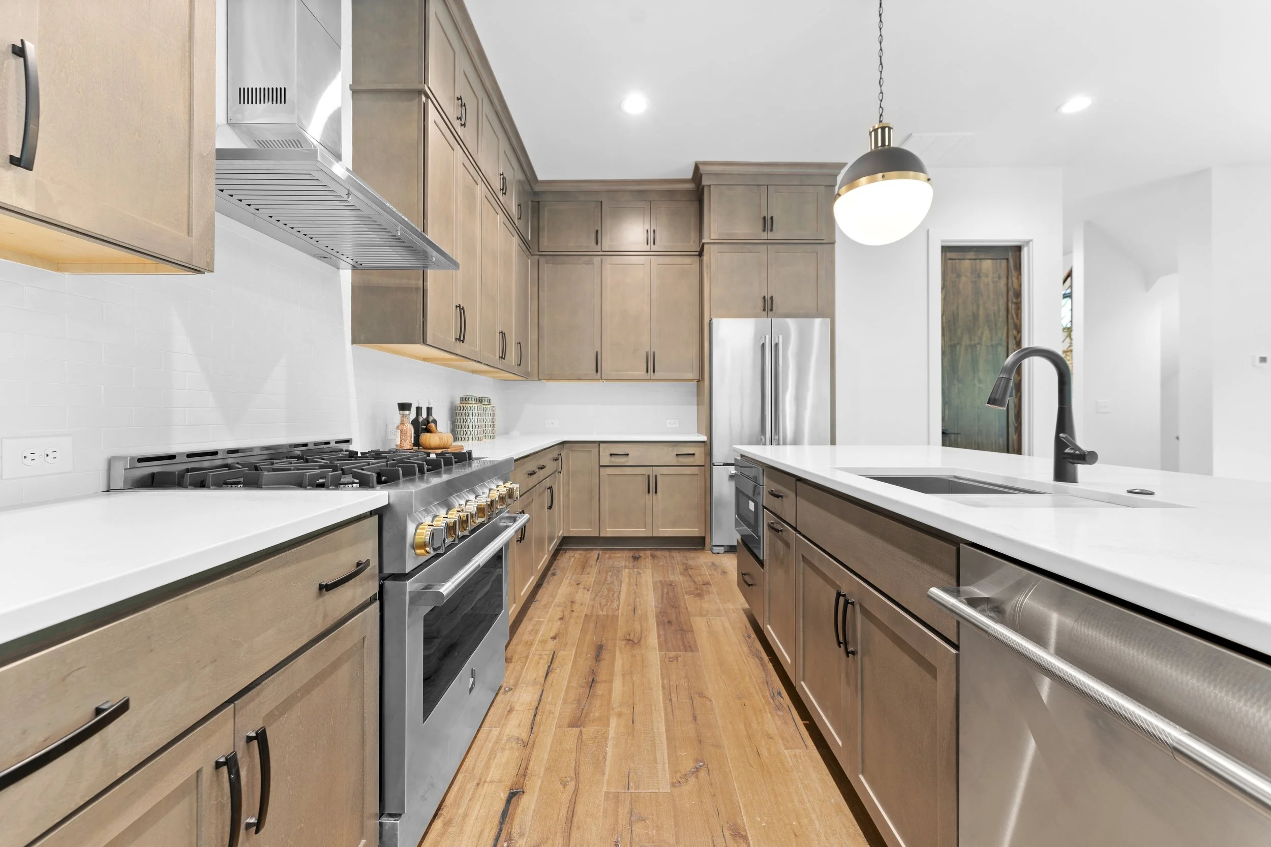 Modern kitchen with wooden cabinets, white countertops, stainless steel appliances, a black faucet, and a hanging pendant light.