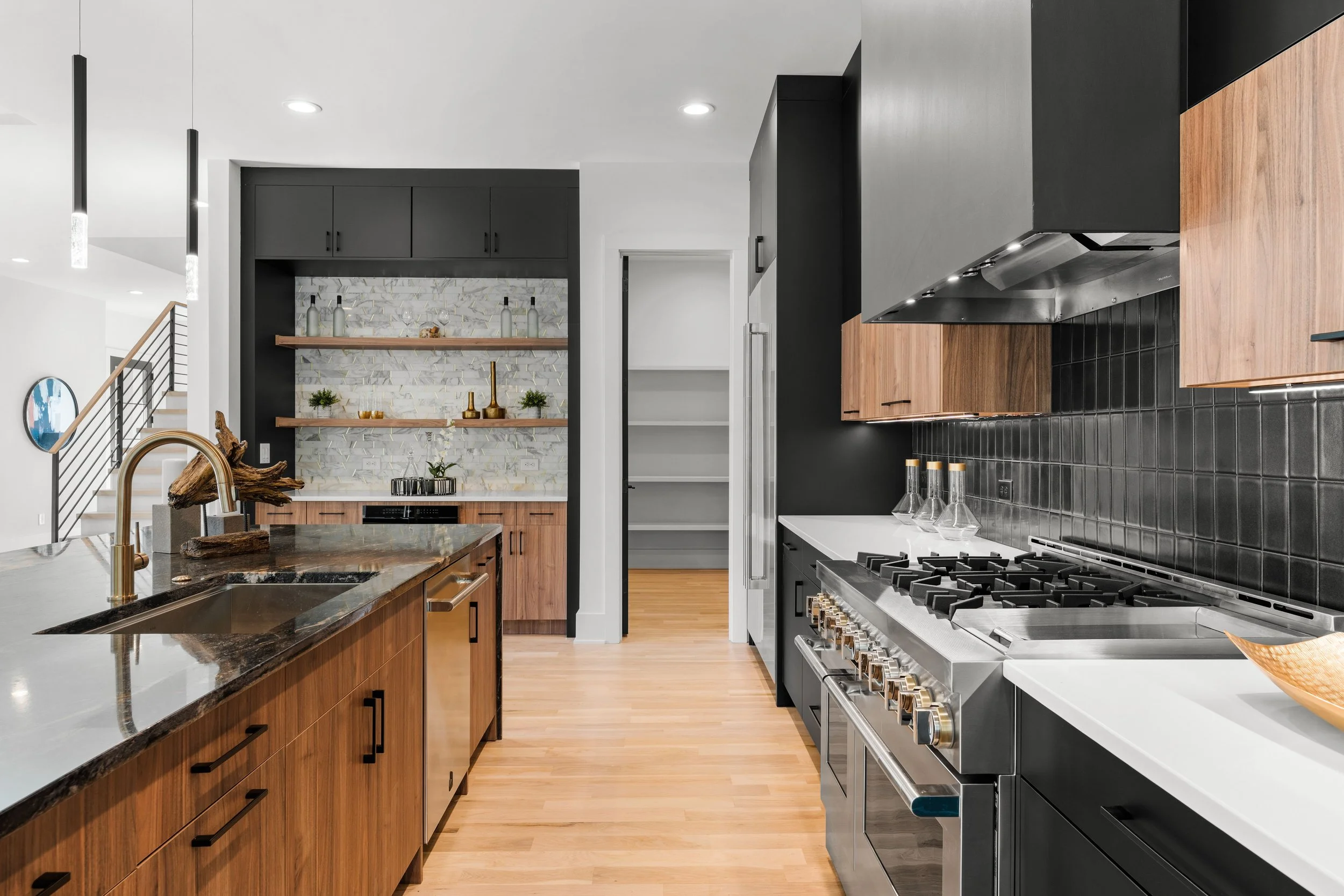 Modern kitchen with wooden cabinets, stainless steel appliances, black backsplash, and open shelving with decorative bottles and plants.