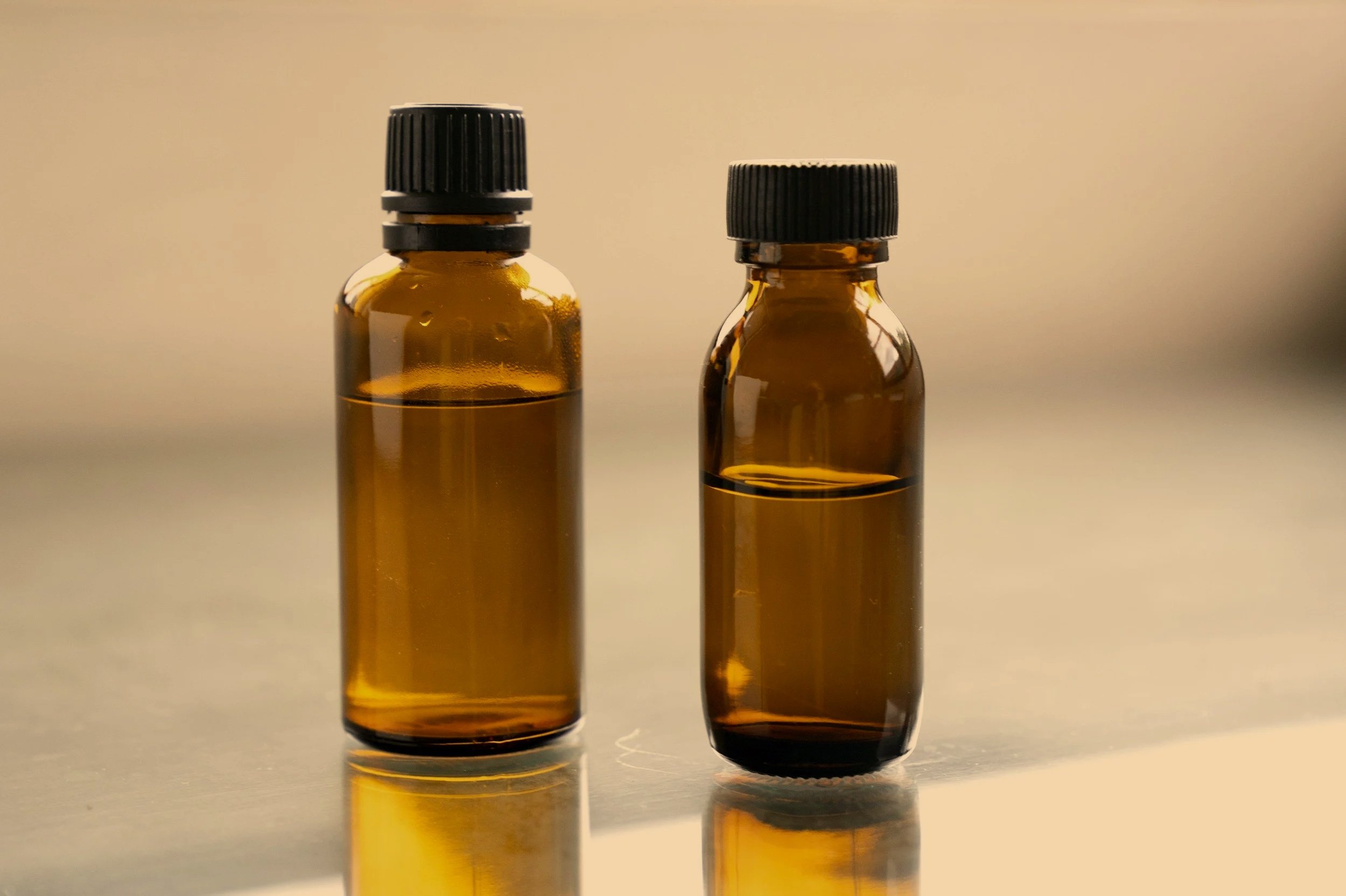 Two small amber glass bottles with black caps, containing liquid, placed on a reflective surface.