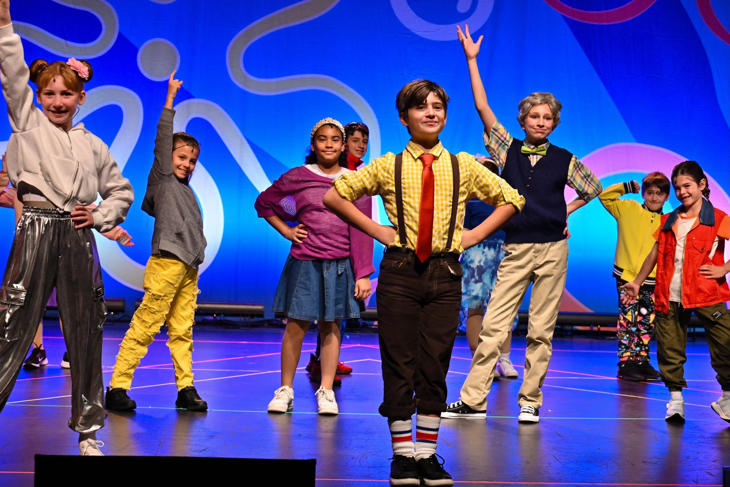 Children performing on stage during a show, dressed in colorful costumes and striking poses.