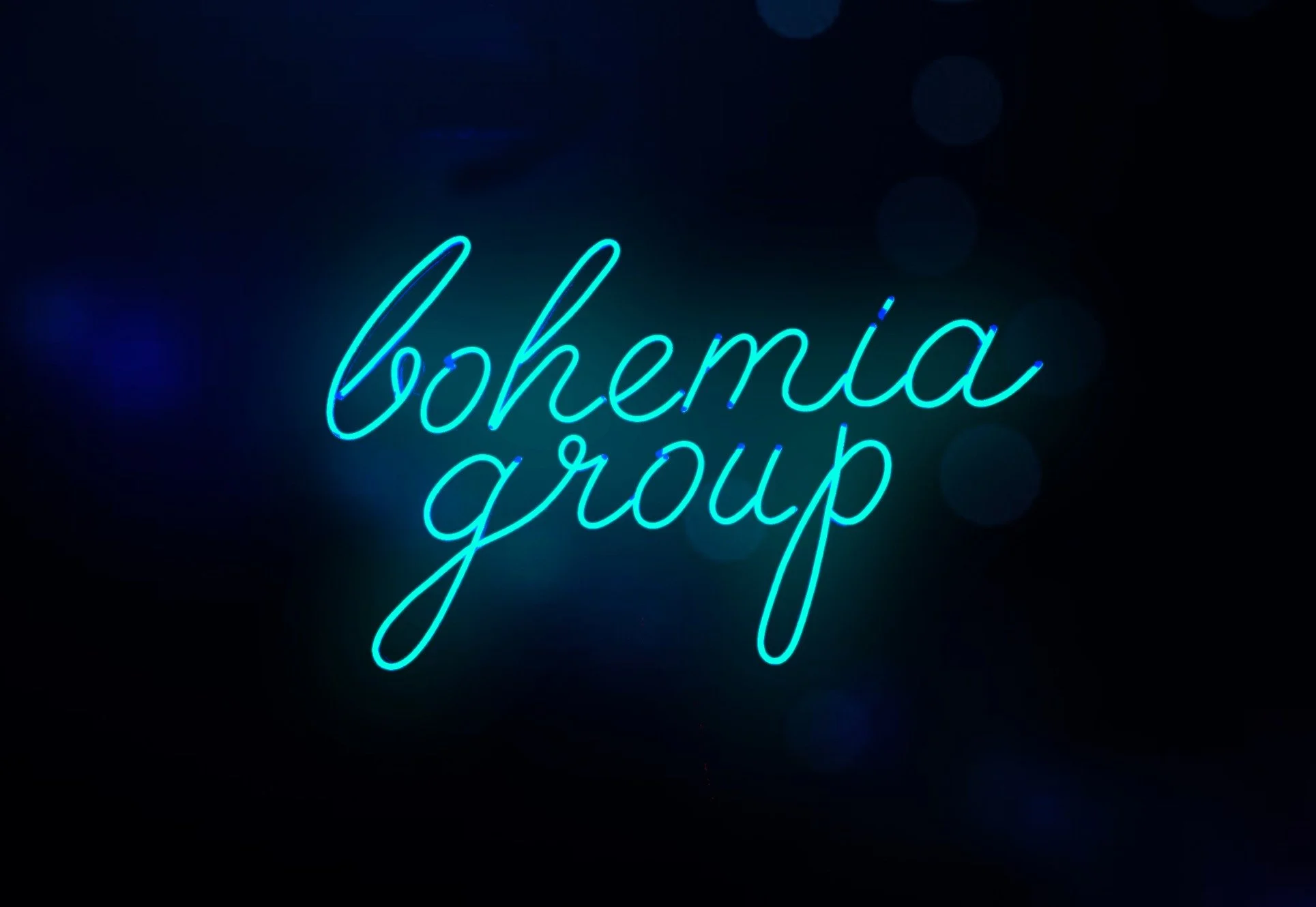 Neon sign reading 'bohemia group' in cursive, glowing blue against a dark background.