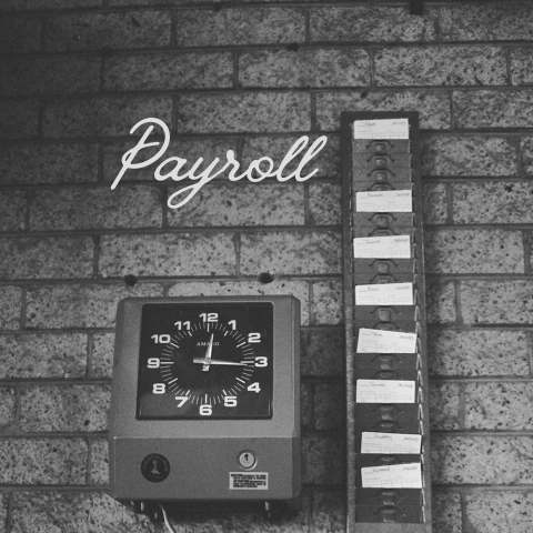 Payroll concept image with time clock and employee time cards representing payroll tracking and employee hours