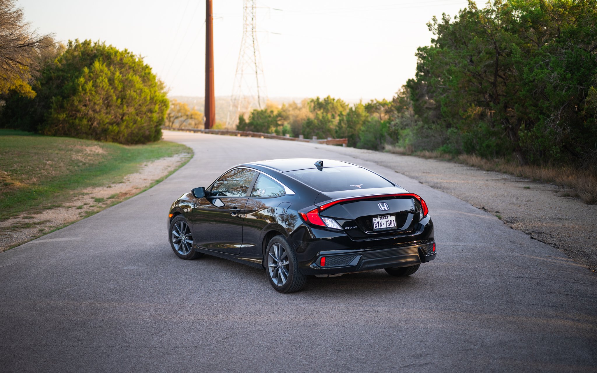 Black Honda Civic parked on a rural road with trees and utility poles in the background.