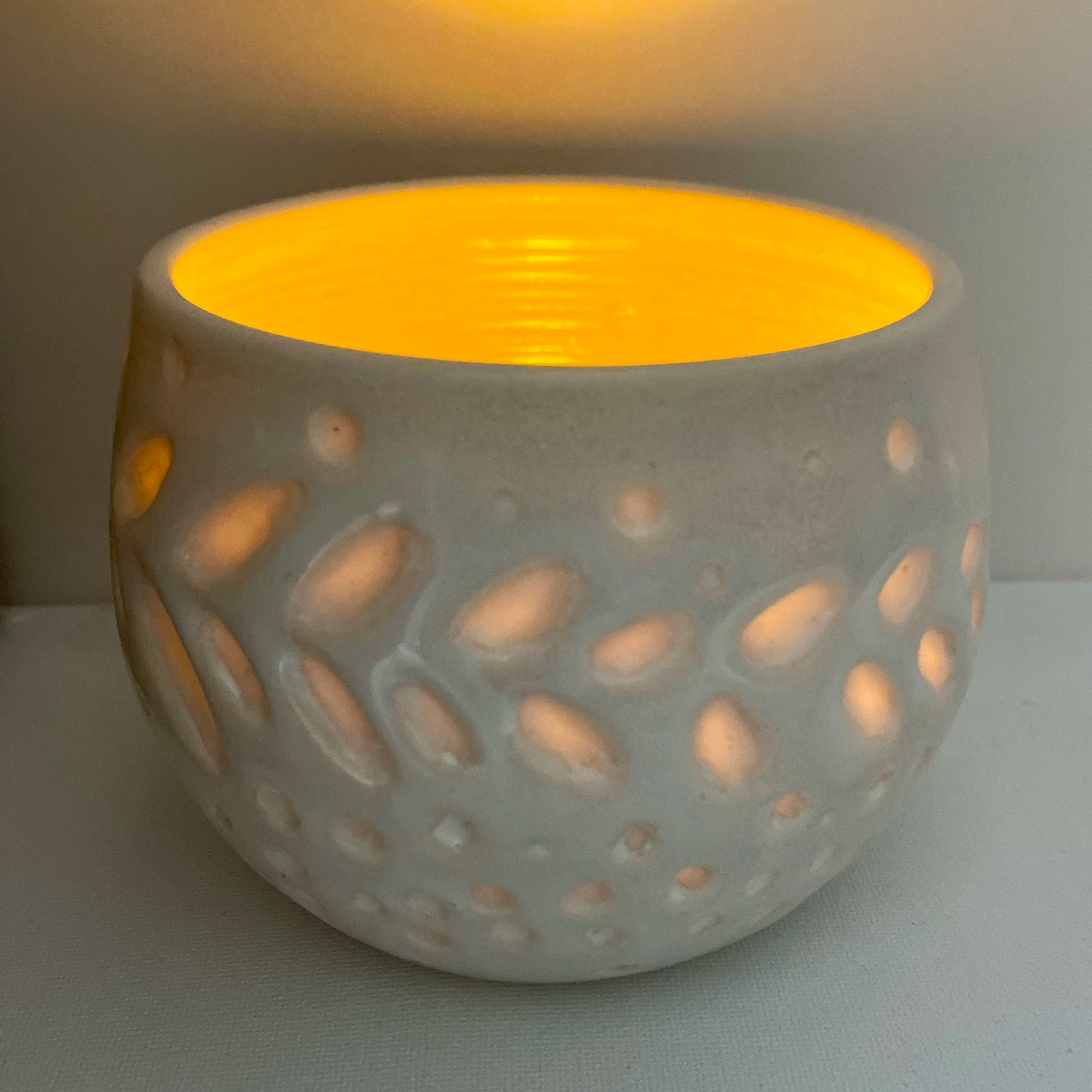 small white candle dish carved with translucent leaves and circles with lit candle