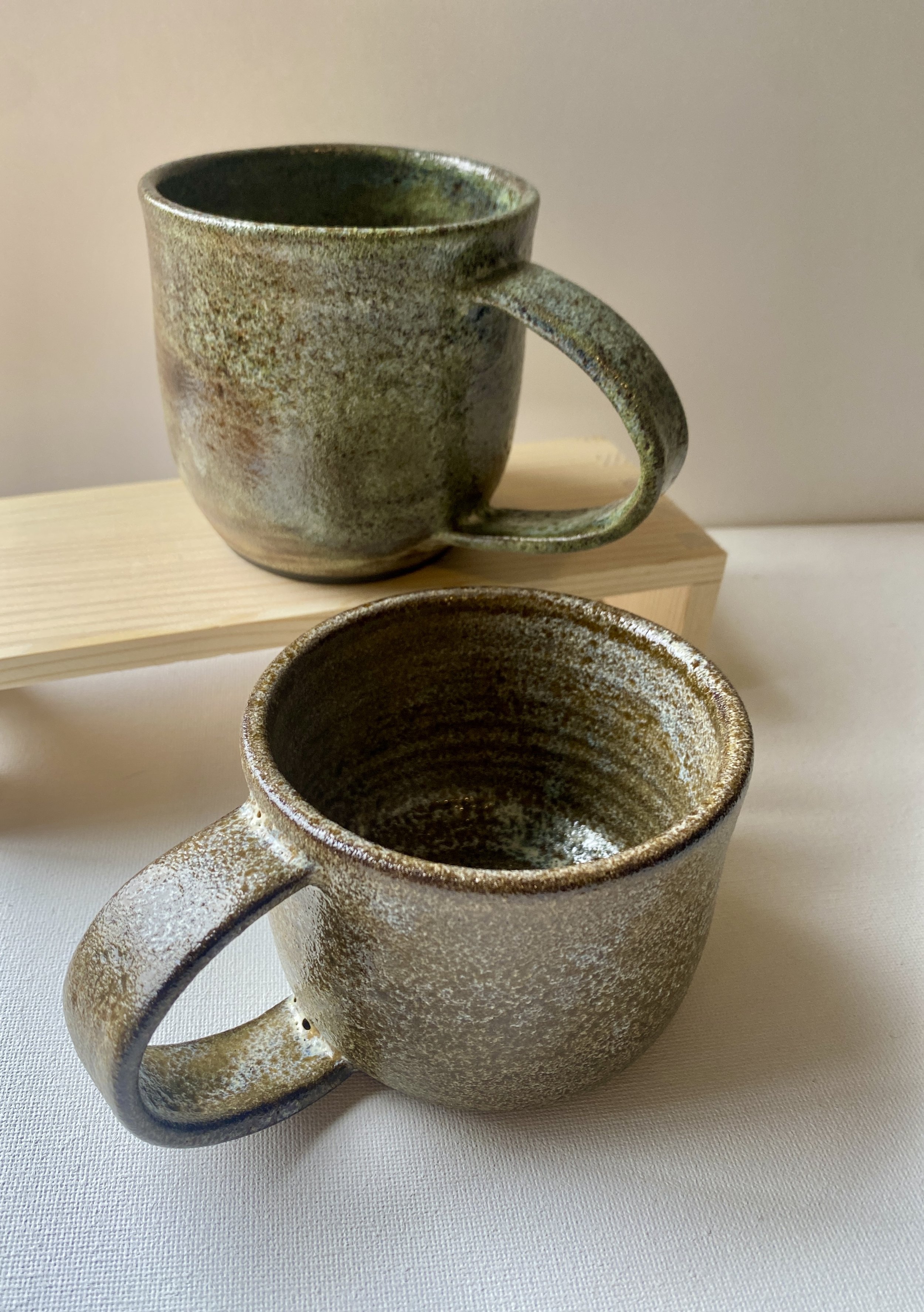 two brown and green mugs, one on a wood stand