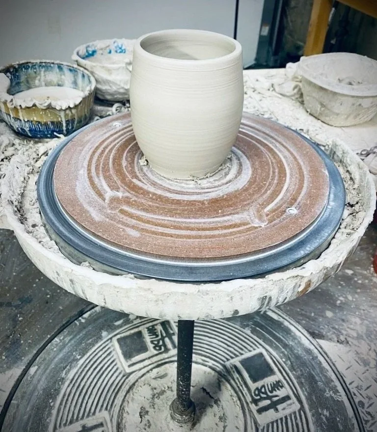 wet clay vase on kick wheel with three bowls of clay water and scraps