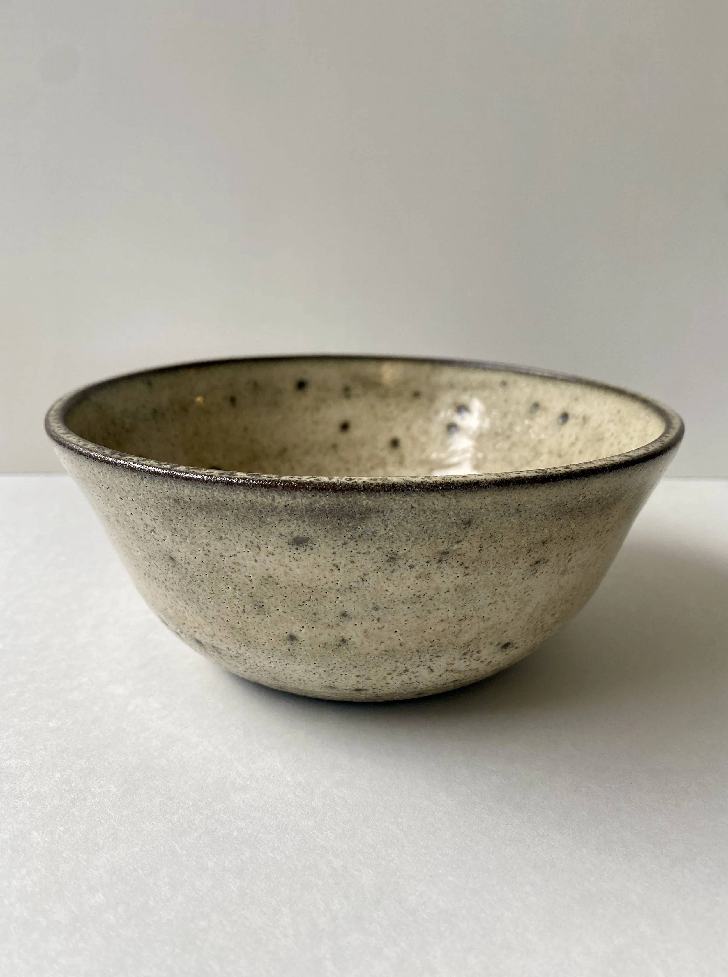 view 1 from the side of a bowl with speckled cream and yellow glaze over black clay