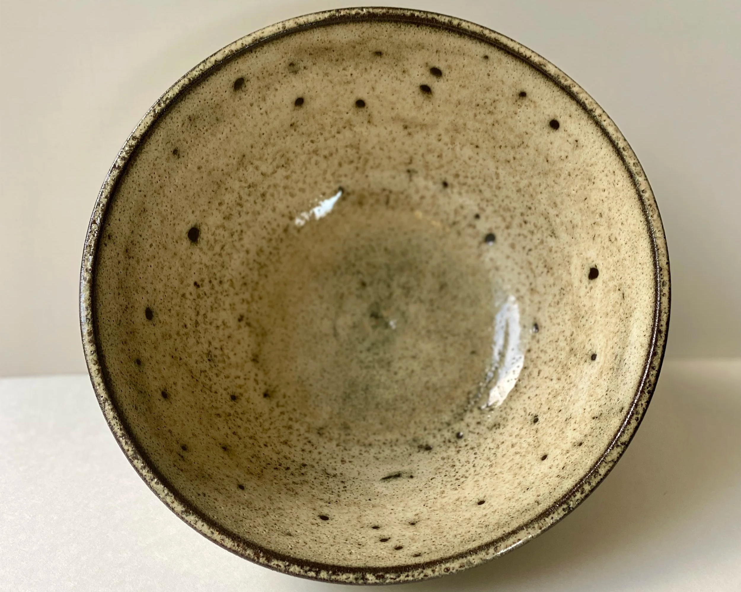 view 2 from the top of a bowl with speckled cream and yellow glaze over black clay