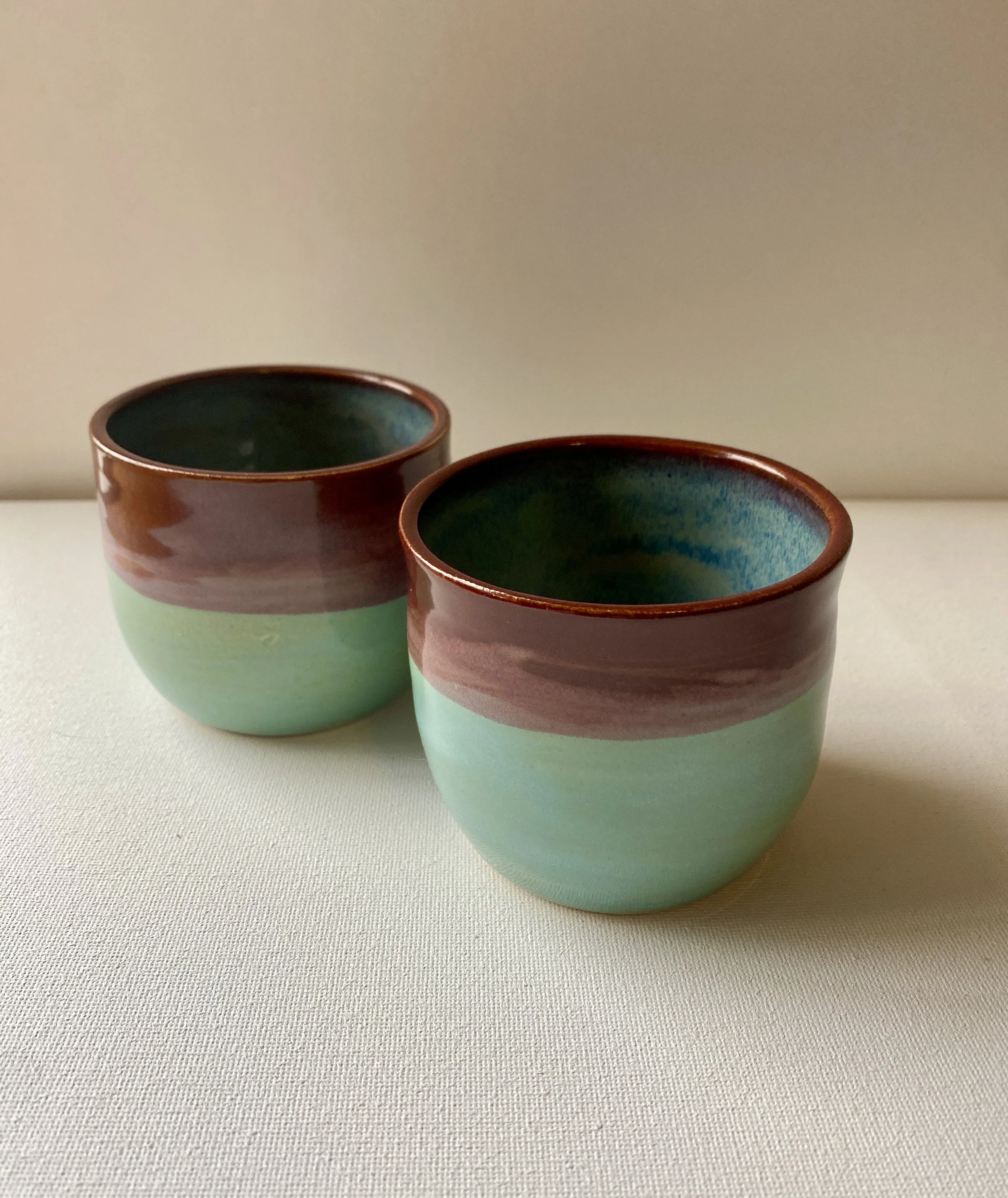 front view of two handleless mugs with reg top half, light blue bottom, and deep blue interior