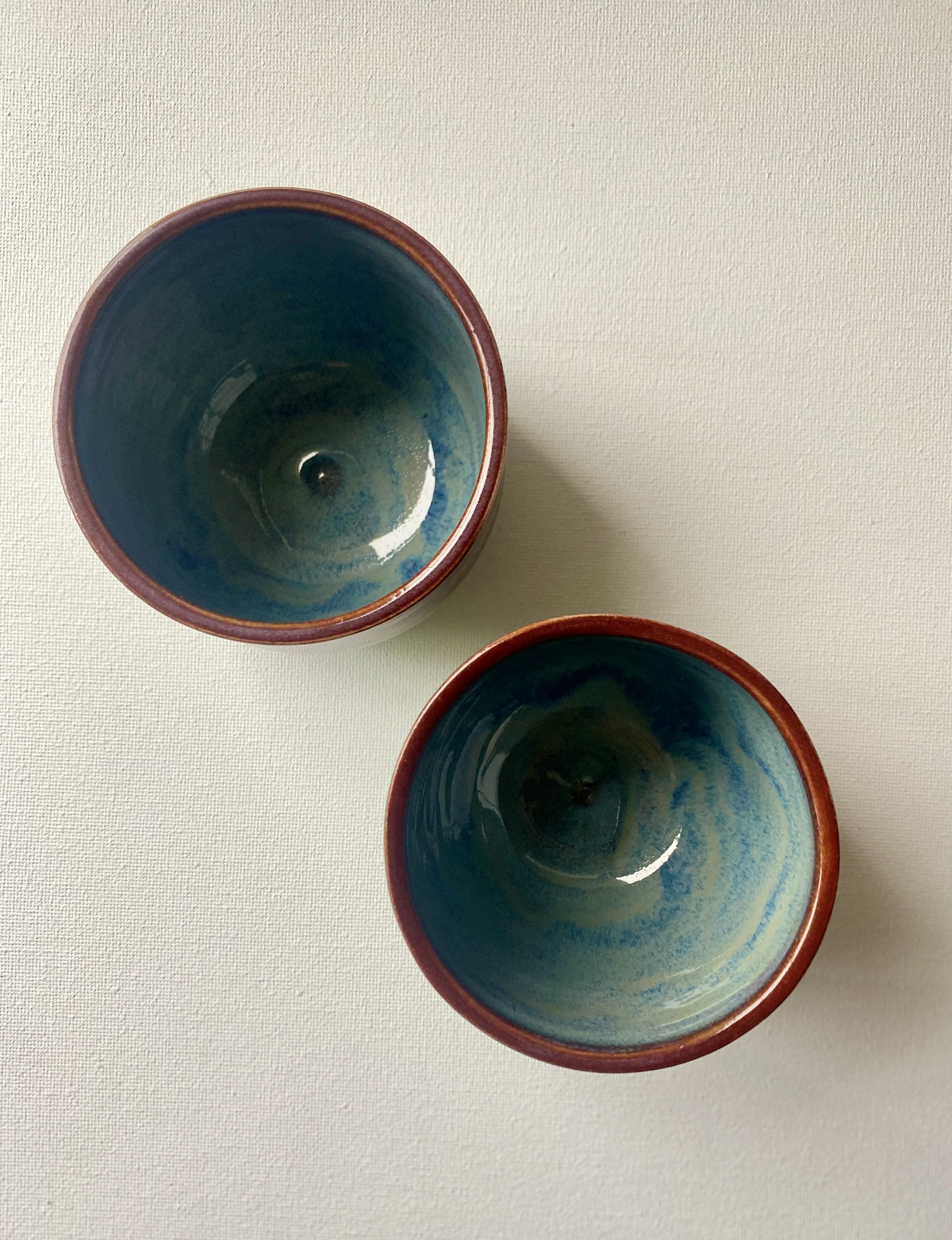 top view of two handleless mugs, red trim with deep blue interior