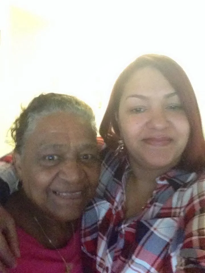 Two women smiling, one older with gray hair and the other younger with reddish-brown hair, pose together for a selfie indoors.