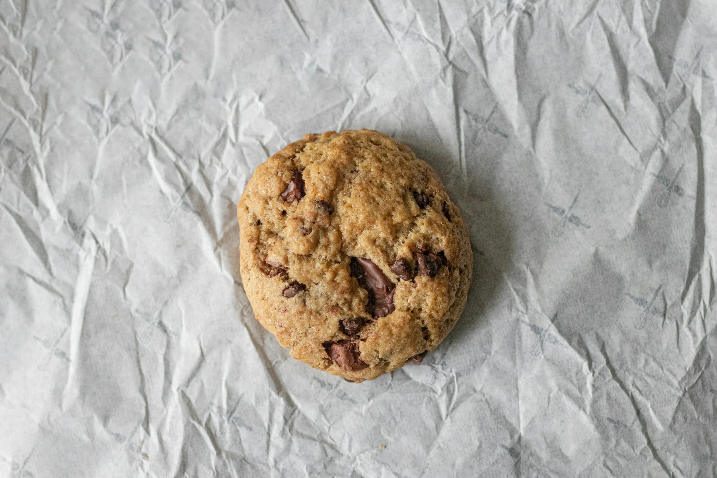 Close-up of a chocolate chip cookie on crumpled parchment paper.