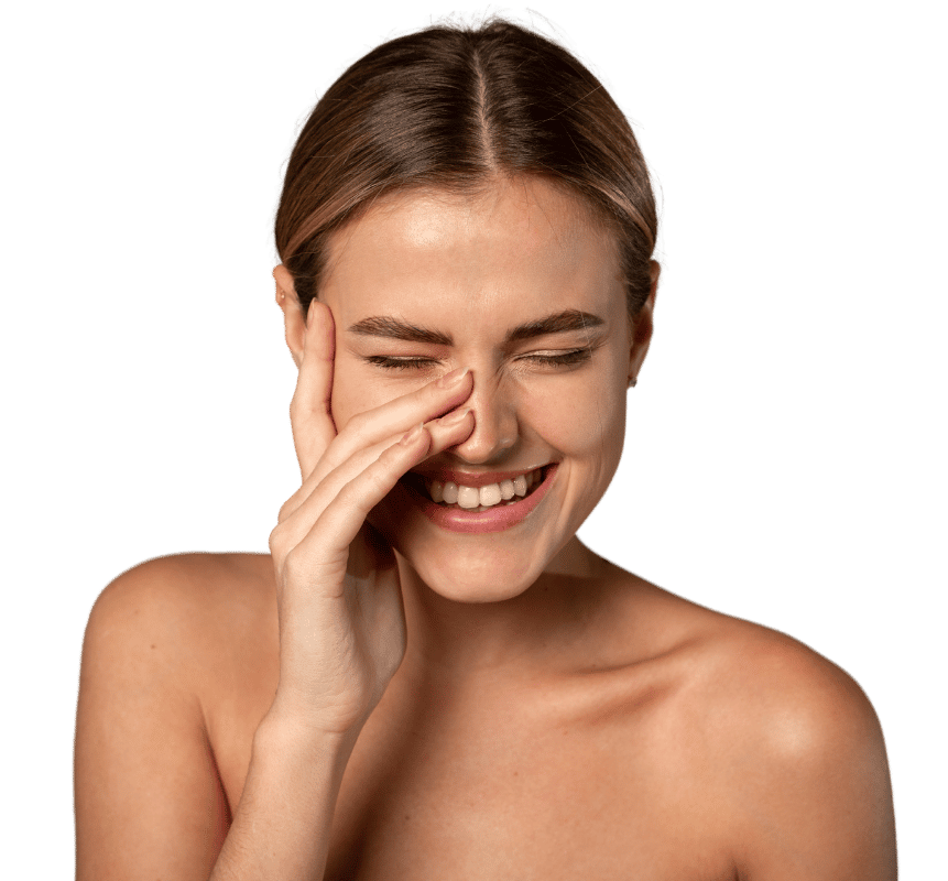 A woman with light brown hair smiling and covering part of her face with her hand, eyes closed, against a plain black background.