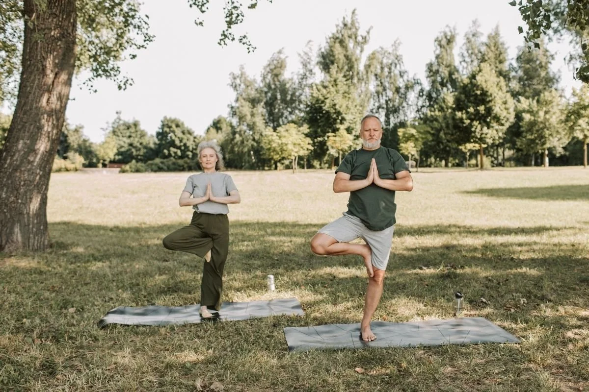 Two older adults practicing yoga outside.