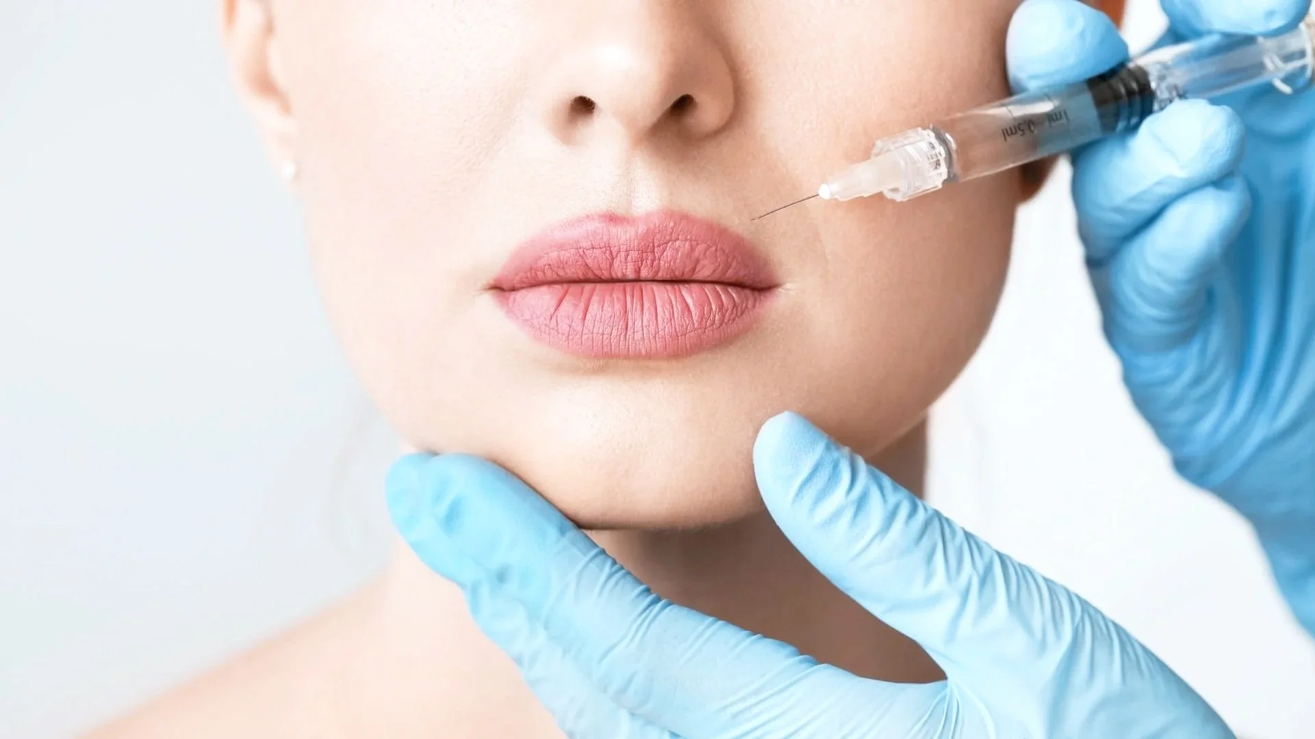 Close-up of a woman receiving a facial injection of cosmetic filler, with a healthcare professional using gloved hands to perform the procedure.