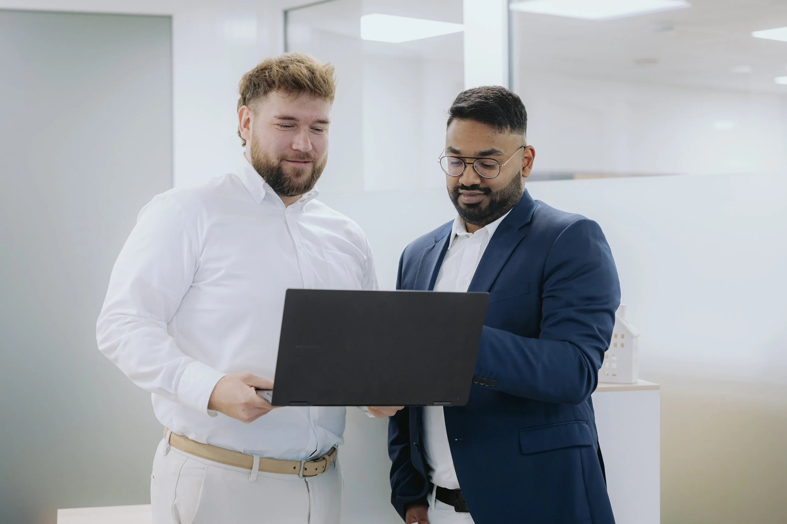 Zwei Männer in Businesskleidung schauen auf einen Laptop in einem modernen Büro.
