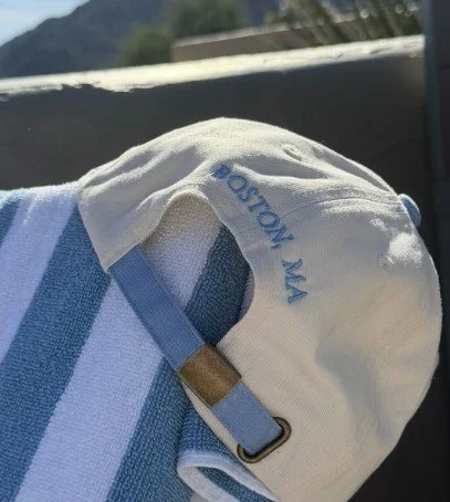 Close-up of a person's shoulder with a white baseball cap and a blue-striped shirt, with a strap from a bag or backpack visible.