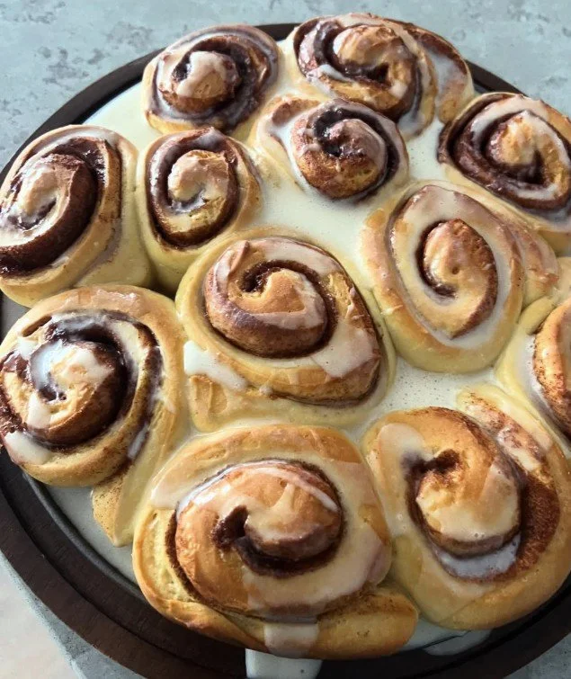 A tray of cinnamon rolls with cinnamon swirls, topped with cream cheese frosting.