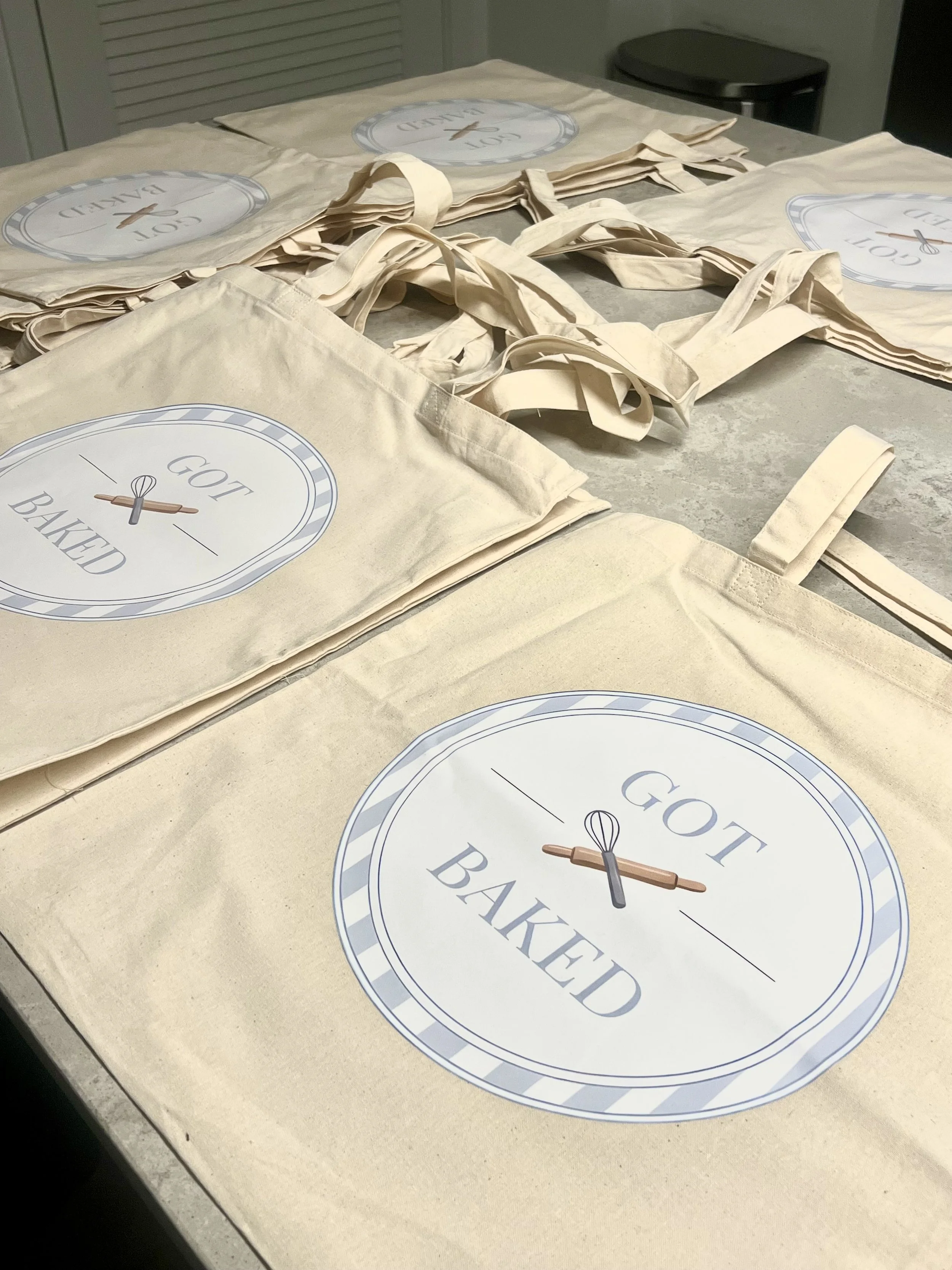 Multiple reusable tote bags with a "Got Baked" logo, placed on a countertop.