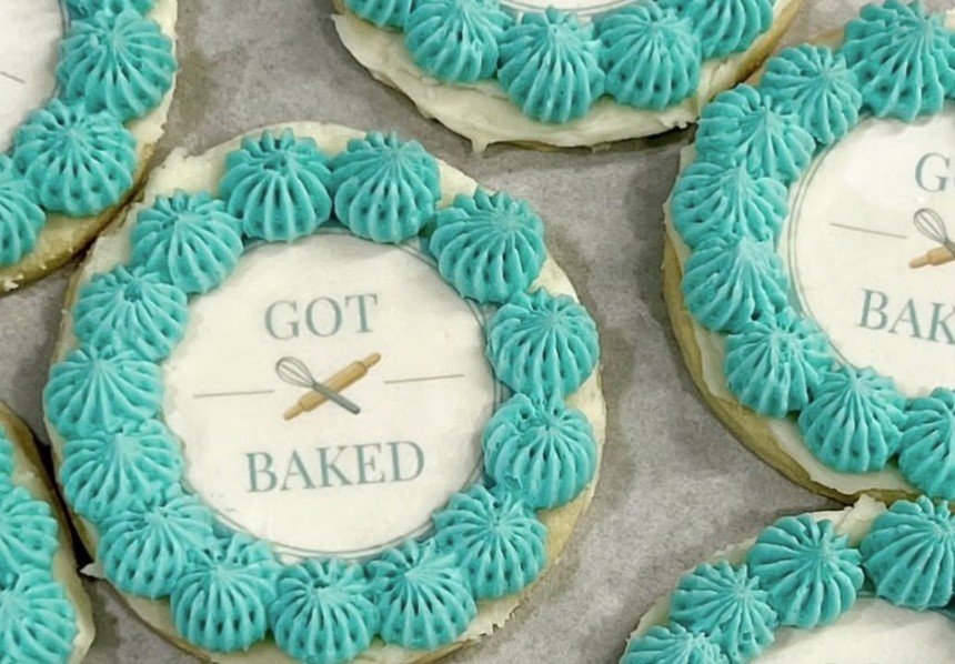 Decorated sugar cookies with teal frosting in a piped pattern, featuring a central edible design with the text 'Got Baked' and a whisk and rolling pin graphic.