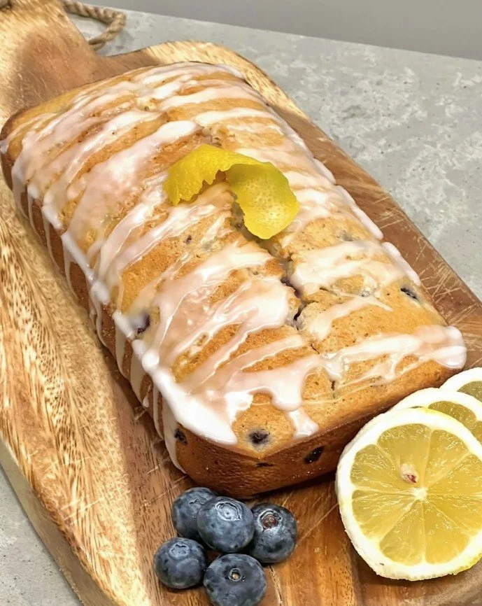 Lemon blueberry loaf cake drizzled with glaze, garnished with lemon slices and blueberries, on a wooden serving board.