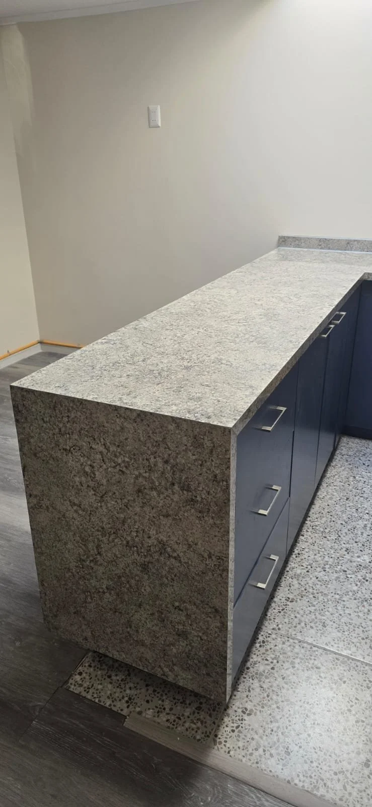 Mostrador de granito gris en una cocina moderna con gabinetes azules y suelo de baldosas decorativas