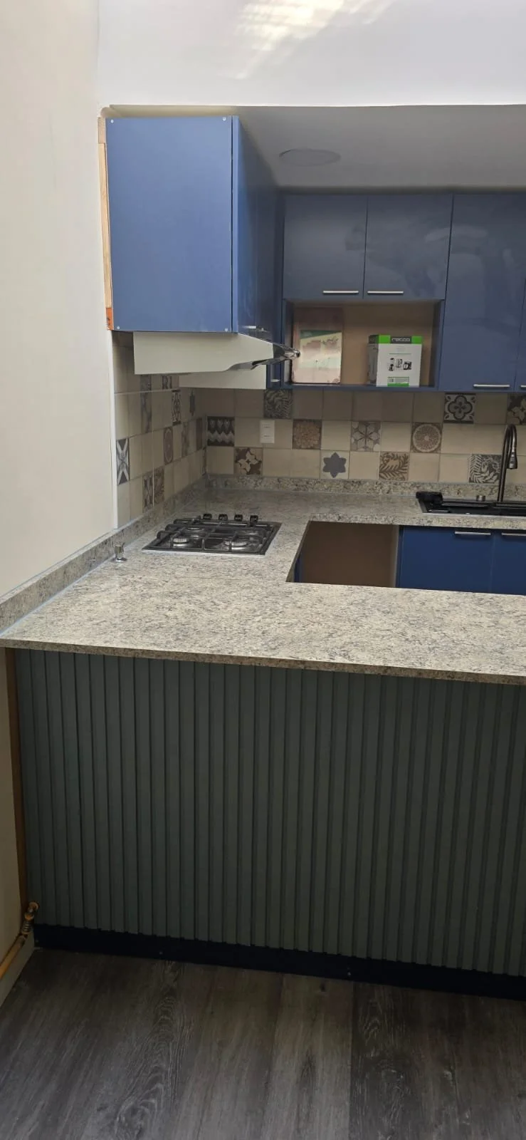 Cocina moderna con gabinetes azules, encimera de granito, salpicadero de azulejos decorativos, estufa de gas y fregadero.