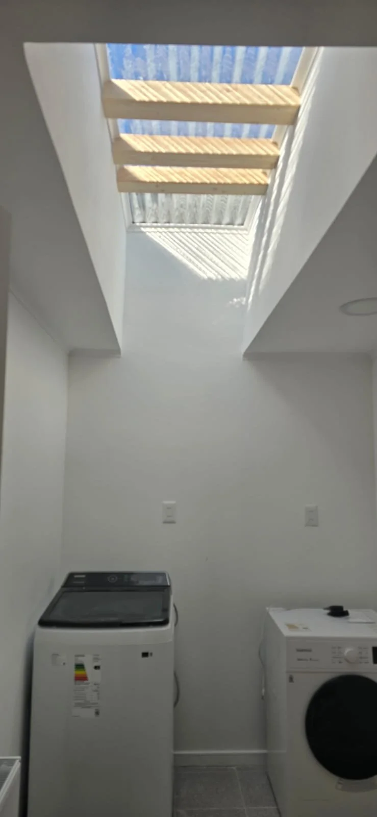 Lavadora y secadora en una lavandería con iluminación natural por un tragaluz.