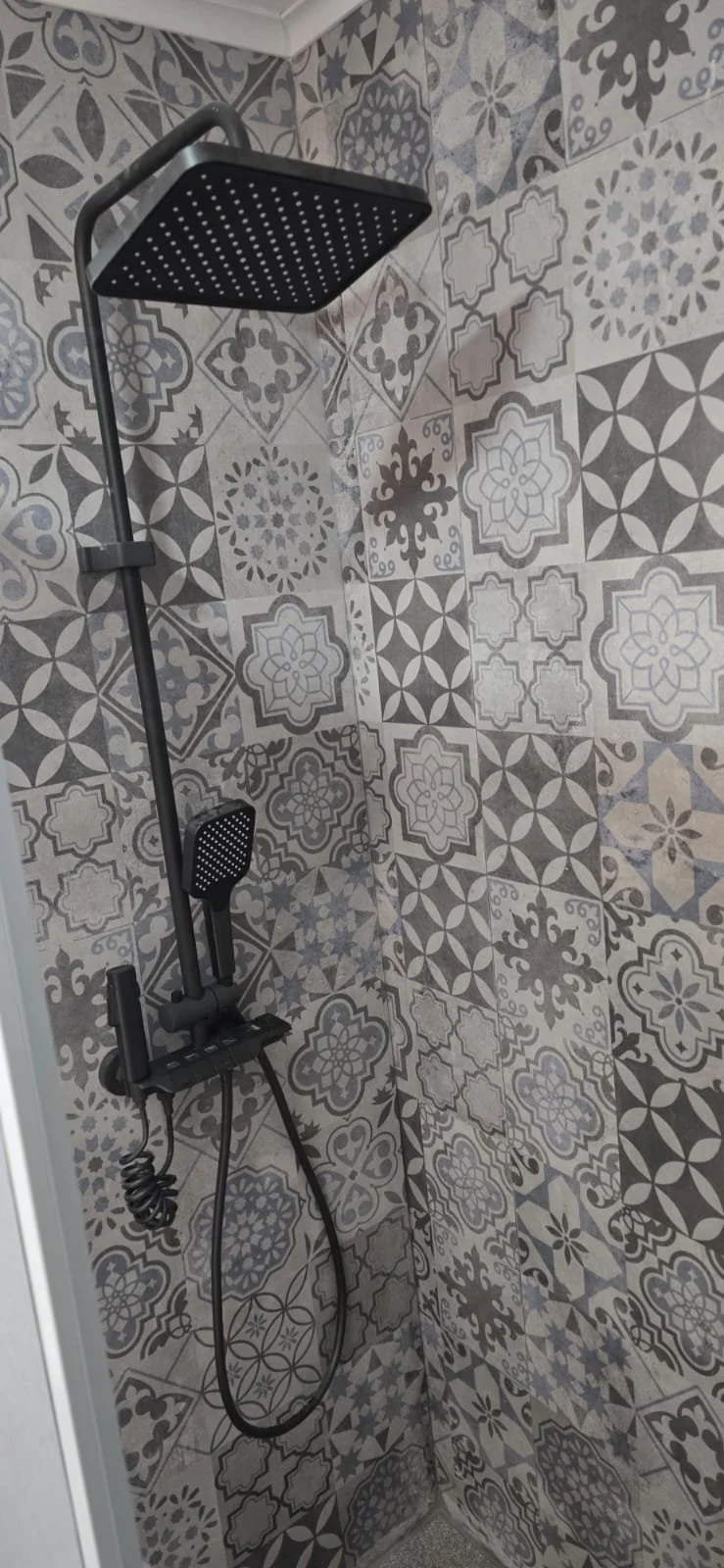 Ducha con azulejos decorativos en tonos grises y negros.