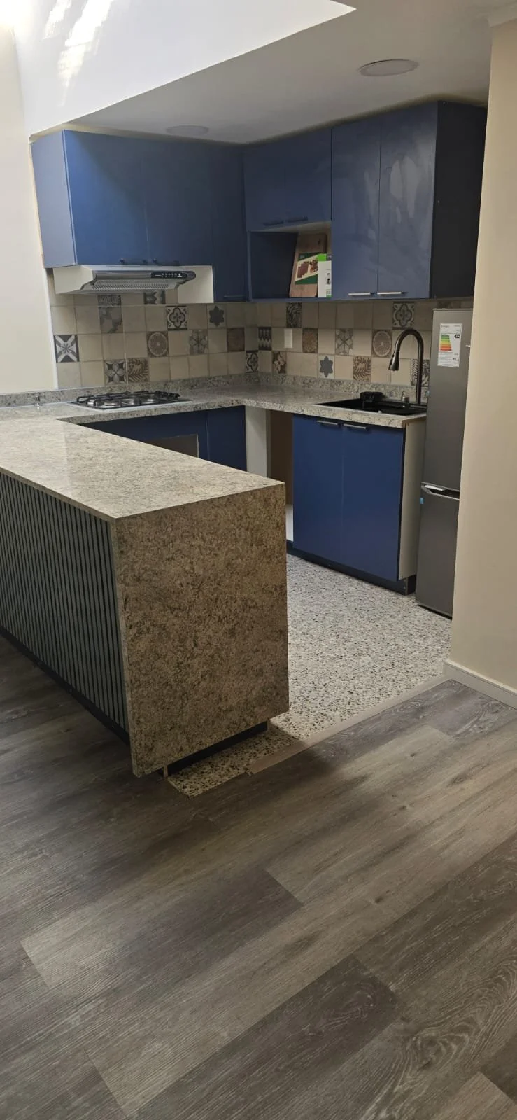 Cocina moderna con gabinetes azules, mesa de granito, pared con azulejos decorativos y electrodomésticos de acero inoxidable.
