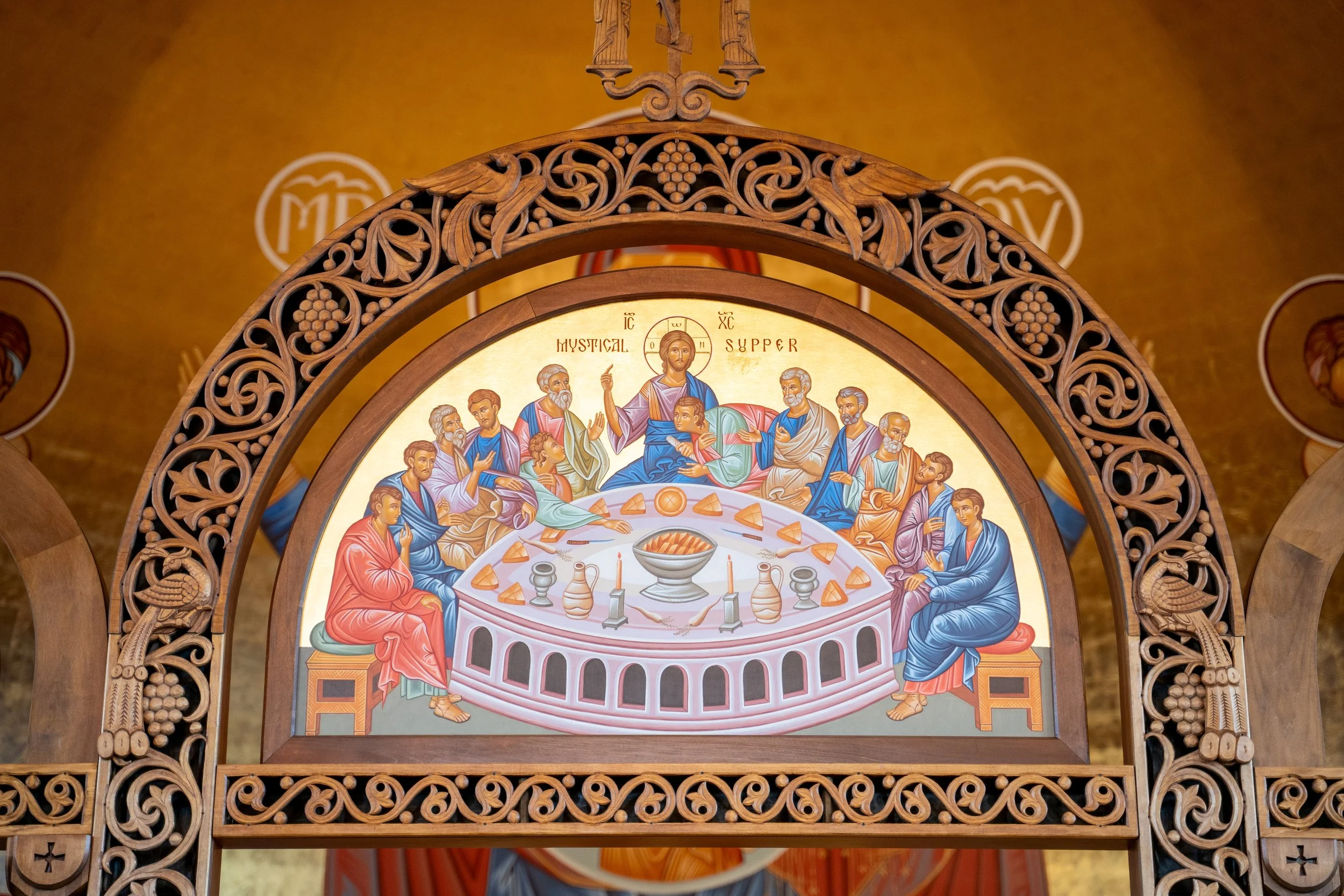 Religious icon depicting Jesus Christ and apostles at the Last Supper, framed by a detailed wooden arch with carved motifs and grapevine designs.