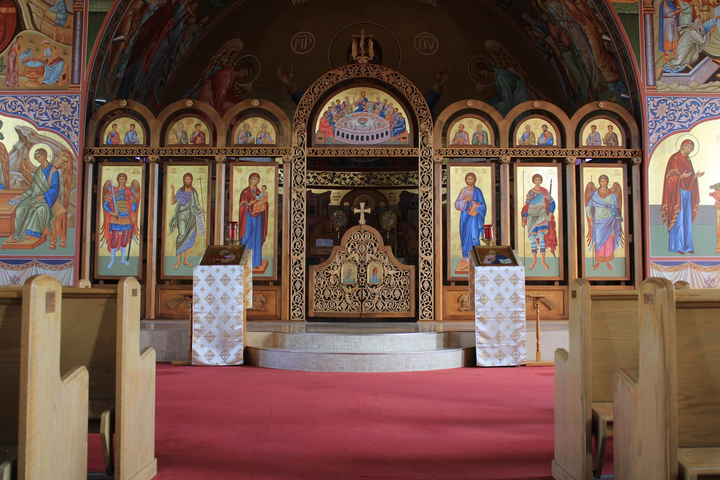 Interior of an Orthodox Christian church altar with colorful religious icons and frescoes, wooden lattice, and altar cloths.