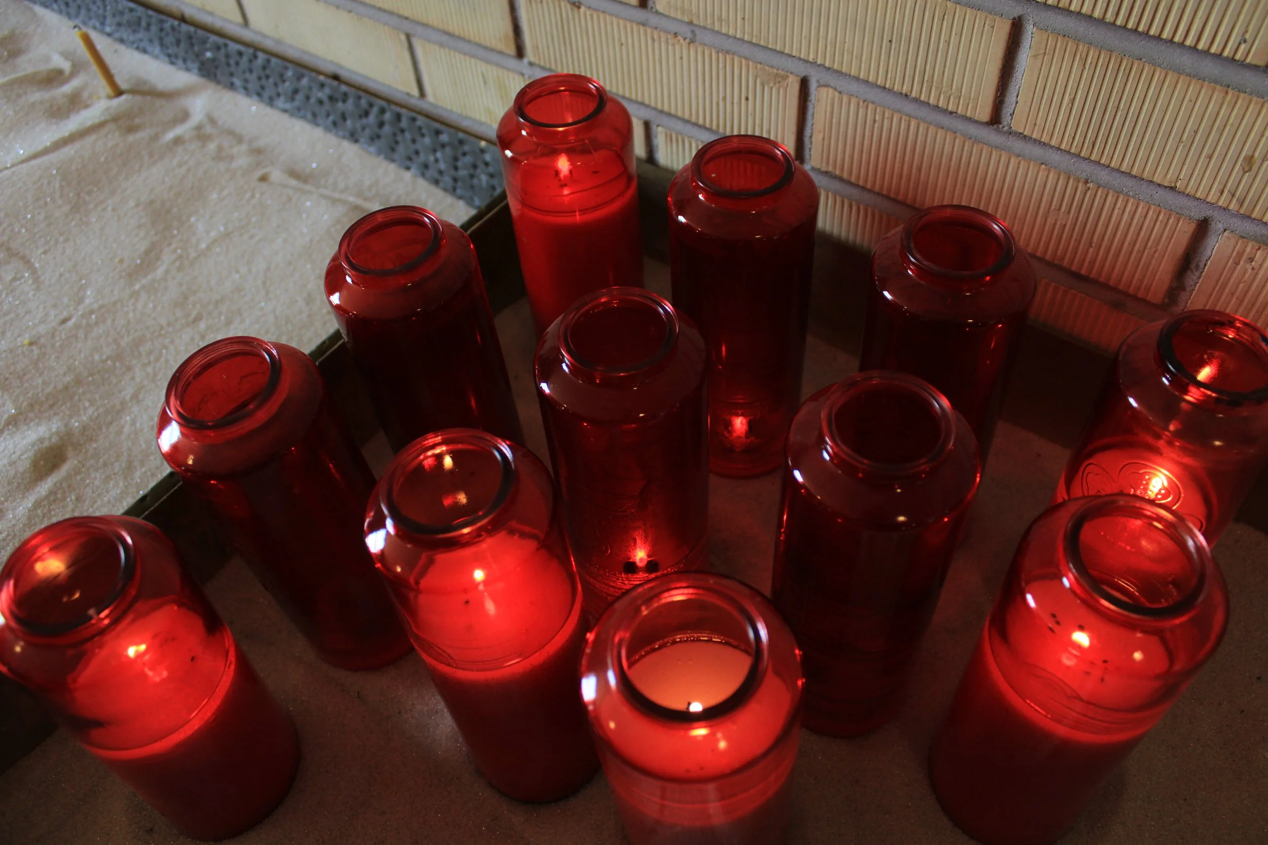 A group of unlit red glass candles arranged on a surface near a brick wall.