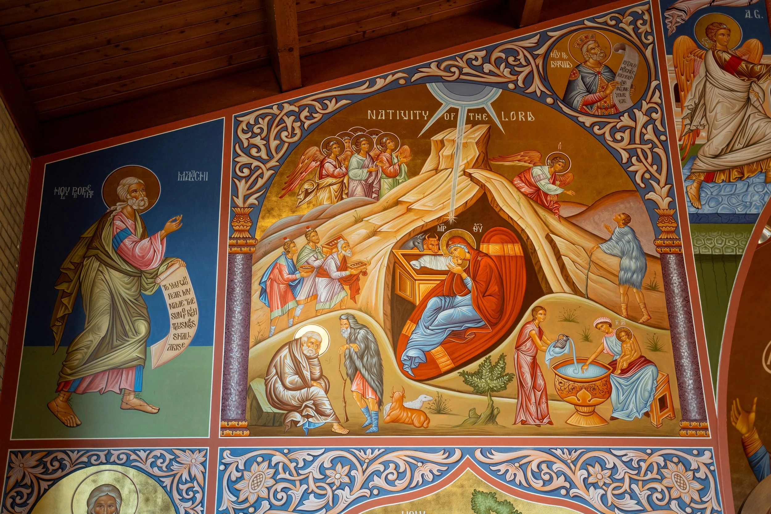 Colorful religious mural depicting scenes from the nativity of the Lord, including angels, saints, and biblical figures, with detailed decorative borders.